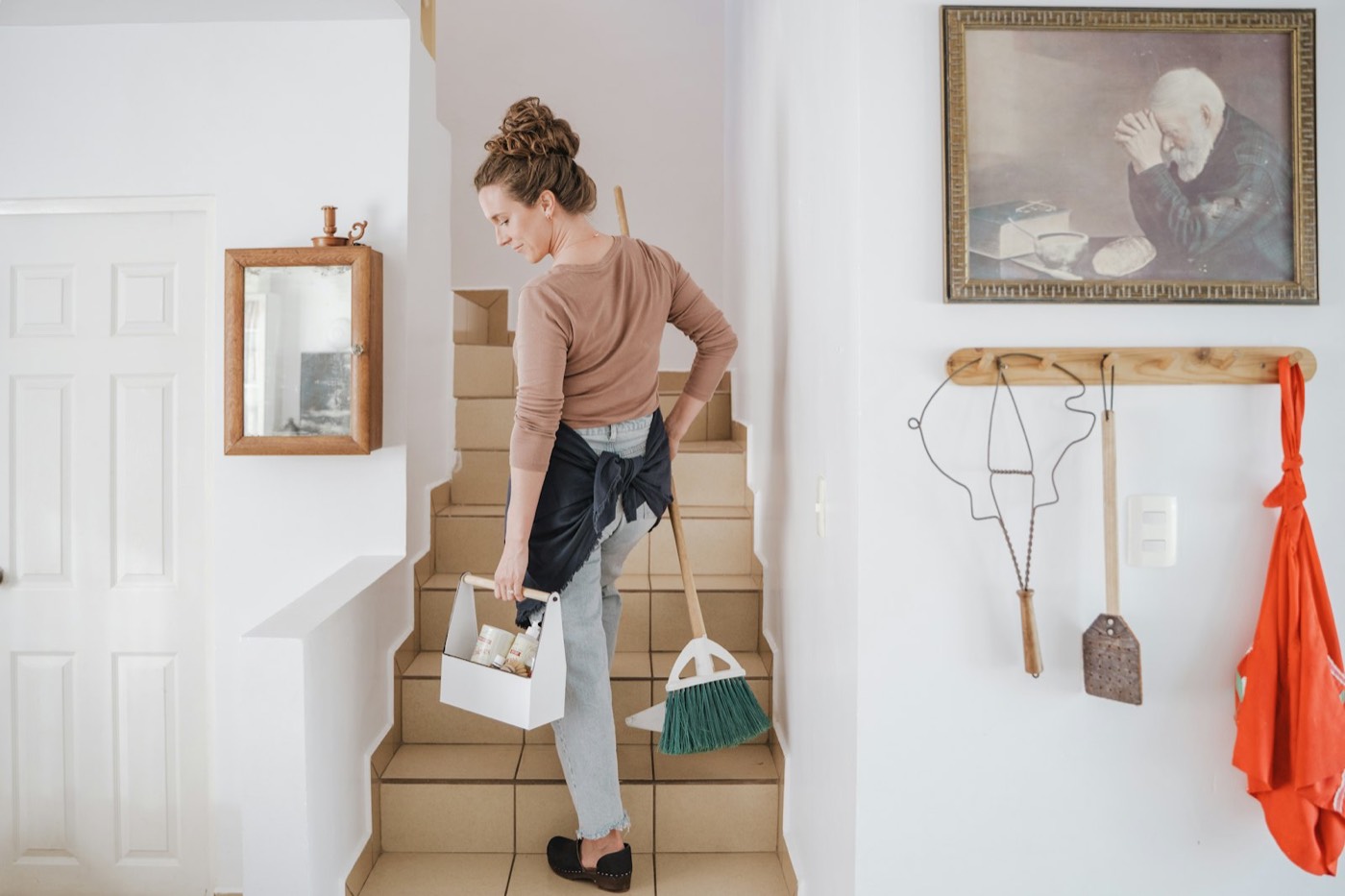 Cleaner carrying a caddy and broom up a tiled staircase