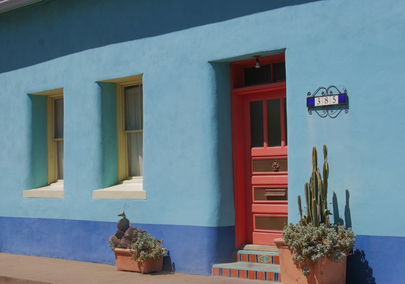Blue adobe-style home with a red door and potted cactus
